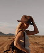 Female model in a utility vest styling the unisex Indy brown felt fedora hat during an outdoor adventure