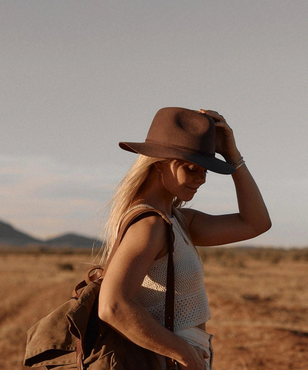 Female model in a utility vest styling the unisex Indy brown felt fedora hat during an outdoor adventure