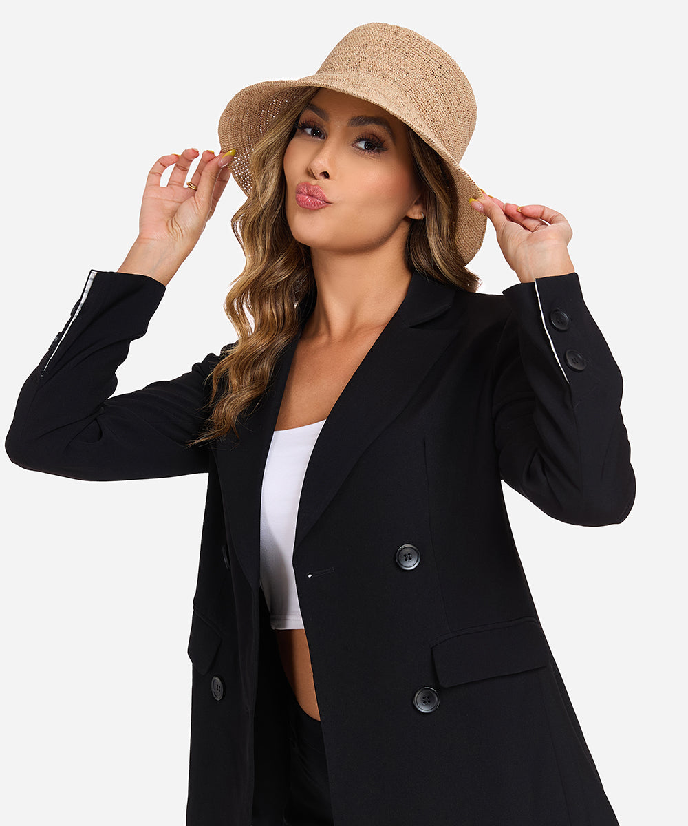 Female model in a sleek black blazer styling the Solstice natural straw packable bucket hat for an elegant summer look